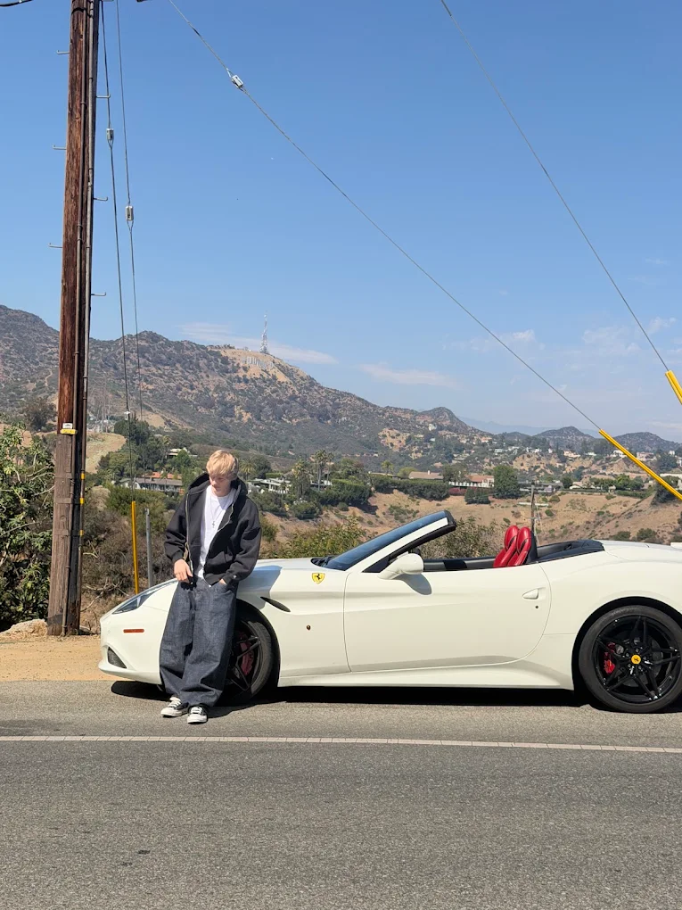 Guest posing beside a white Ferrari California T convertible with the Hollywood Sign in the background during a Ferrari driving experience in Los Angeles.