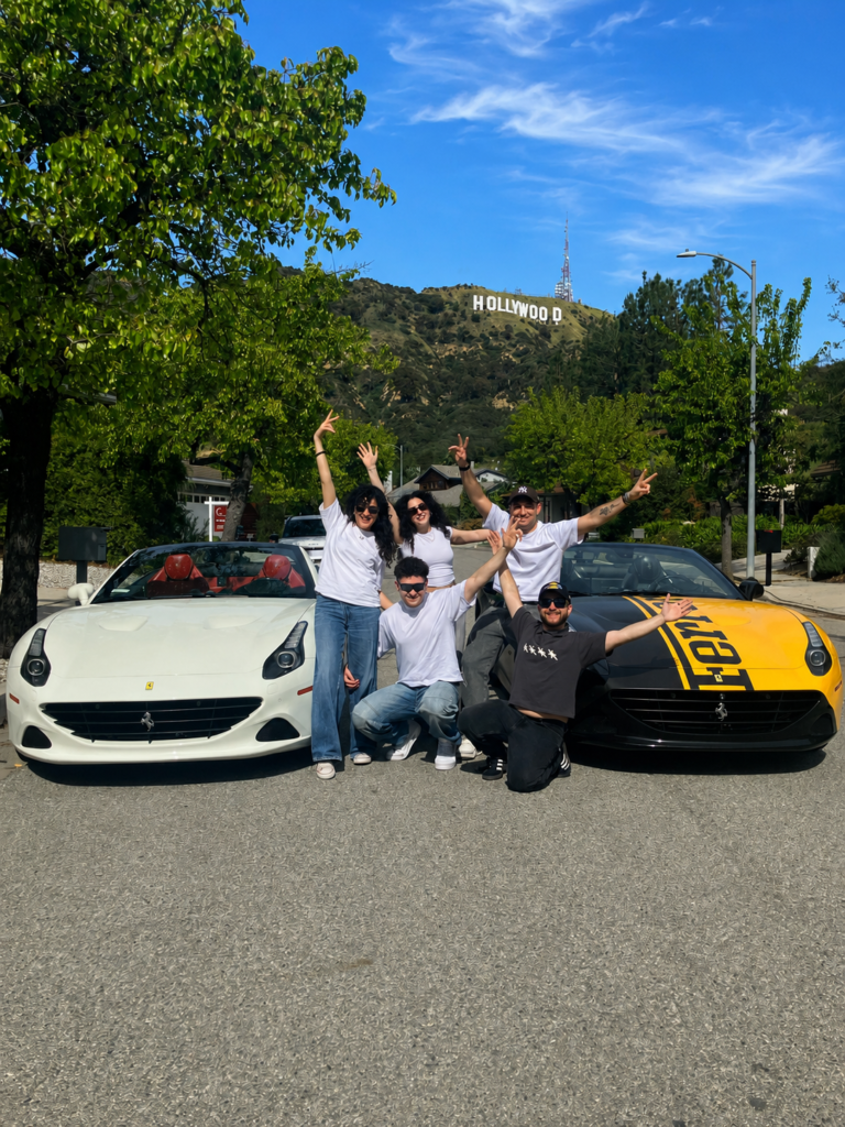 Group posing between two Ferrari California T convertibles with the Hollywood Sign in the background during a Ferrari driving experience in Los Angeles.