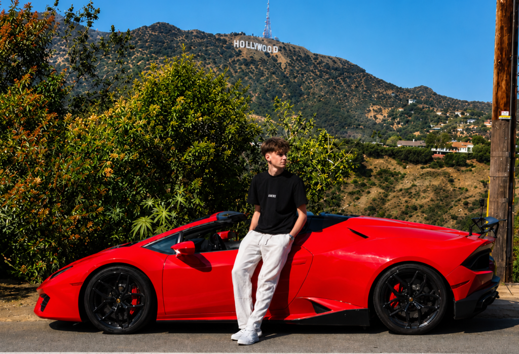 Young man posing beside a red Lamborghini Huracán Spyder with the Hollywood Sign in the background