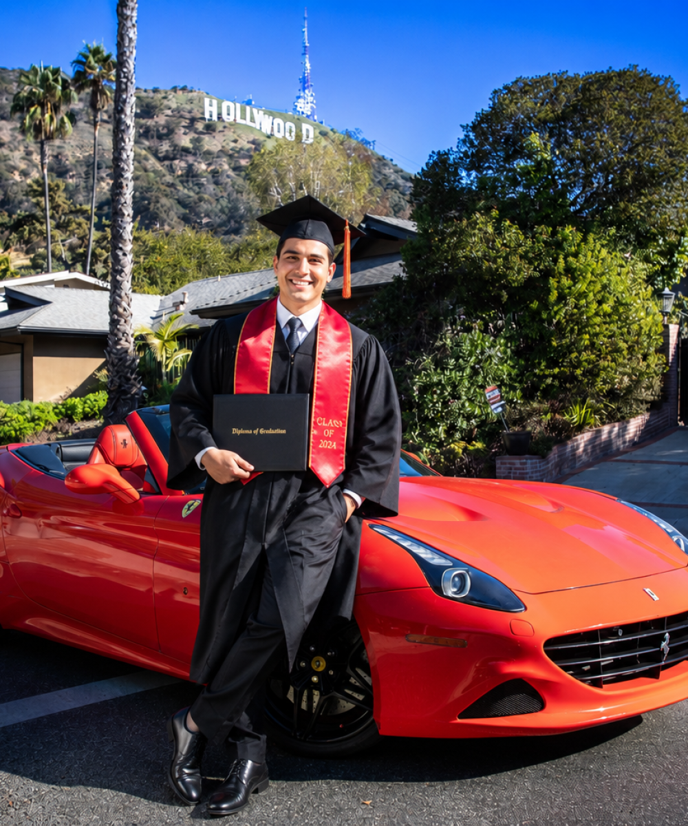 College graduate in cap and gown posing with a diploma beside a red Ferrari convertible near the Hollywood Sign during a graduation celebration experience in Los Angeles.
